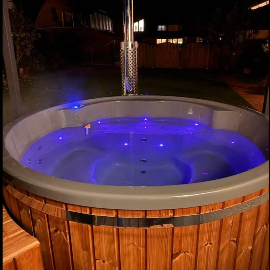 Night view of illuminated wood fired hot tub with blue LED lights and stainless steel chimney in outdoor setting