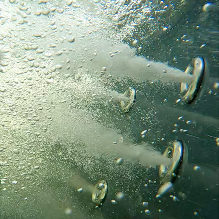 Close-up underwater view of four jet nozzles releasing streams of bubbles into the water