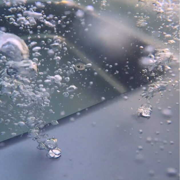 Close-up underwater view of rising air bubbles against a blurred grey surface background.